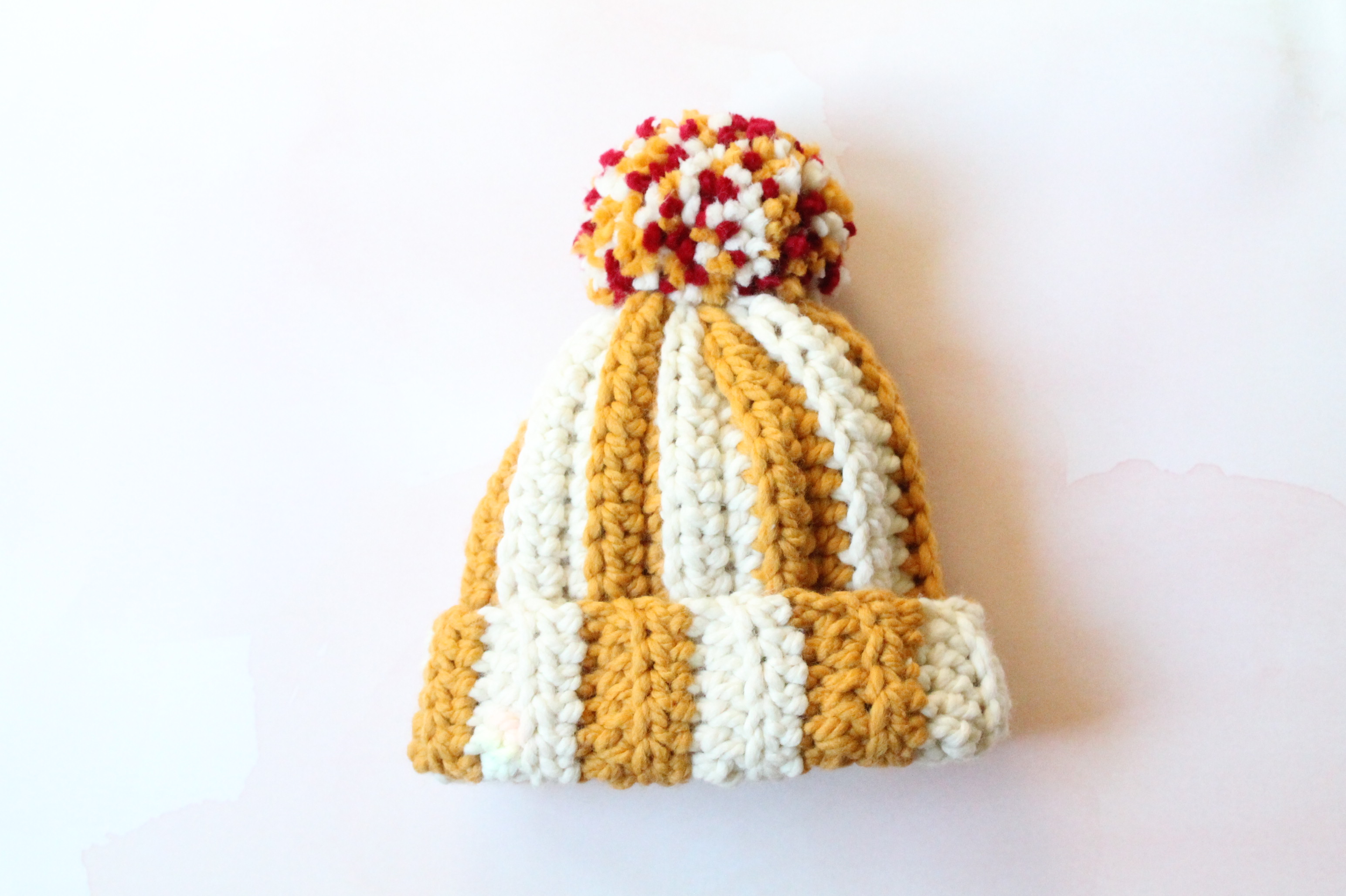 Yellow and white stripe crochet hat with red, yellow, and white oversized pom pom