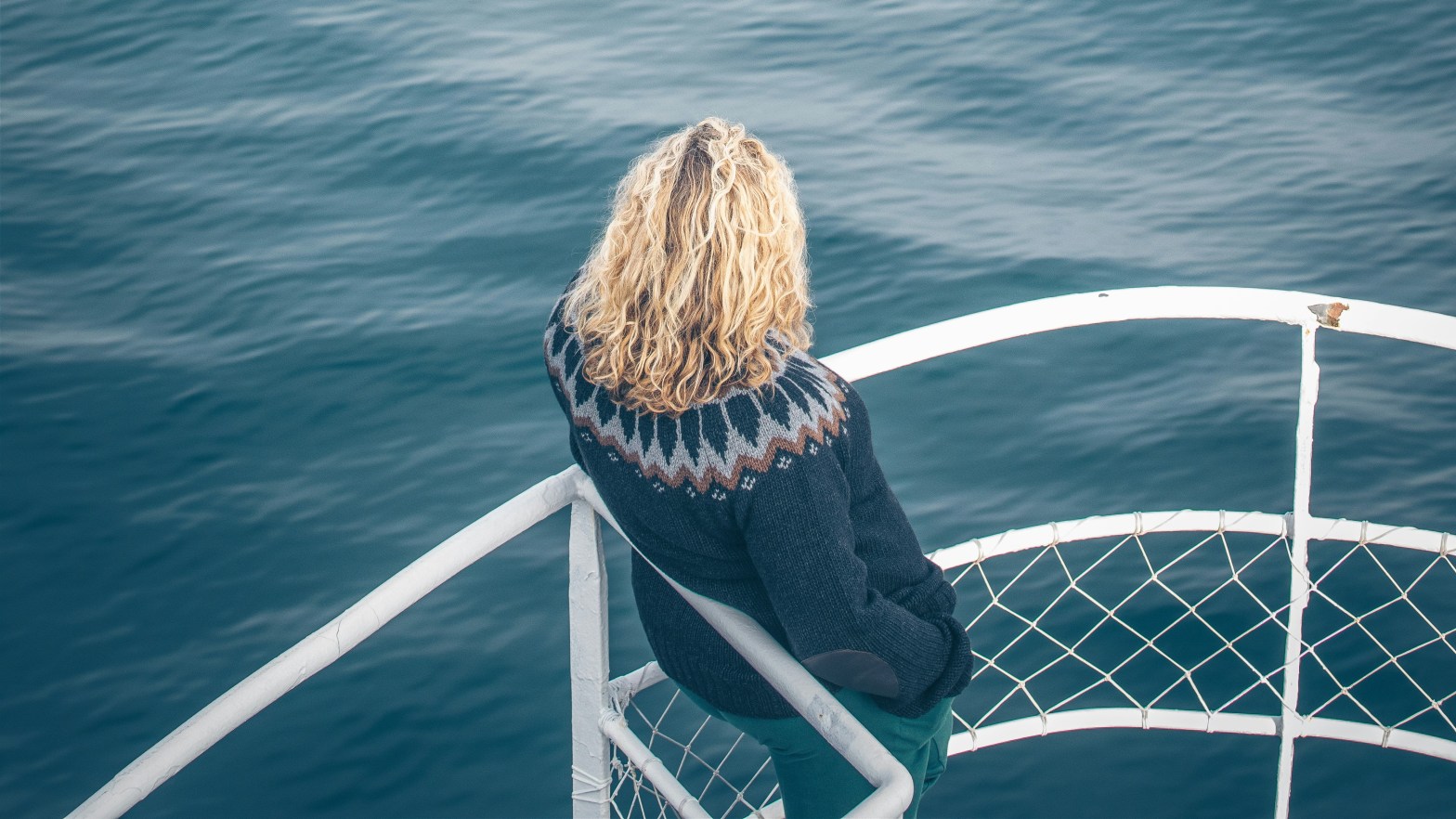 Woman wearing Icelandic knit sweater design, Lopapreysa, stands on boat overlooking water